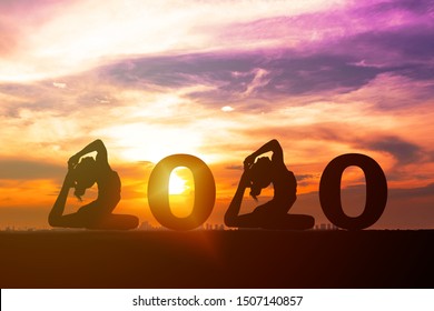 Greeting Card 2020 Happy New Years. Silhouette Of Healthy Young Woman Practicing Yoga And 2020 Years With Sky Sunset. People Doing Yoga Standing Between Numbers 2020. Concept Celebrating New Year.