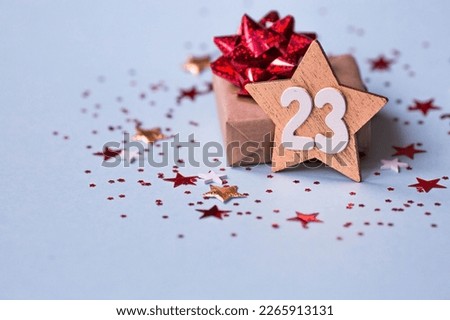 Greeting card for the Defender of the Fatherland Day. White, gold, red stars, a gift box and the number 23 on a light blue background. The holiday is February 23.