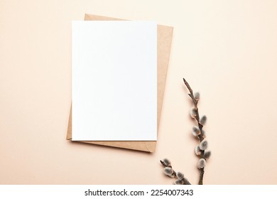 Greeting card mockup with branch of pussy willow and envelop on beige background, top view, flat lay. Blank Easter Holiday card mock up with soft fluffy catkins