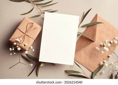 Greeting card mockup with gift box, envelope and eucalyptus and gypsophila twigs on beige background. Card mockup with copy space. - Shutterstock ID 2026214540