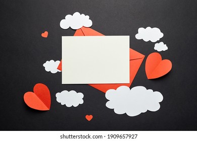 Greeting Card Mockup With Paper Decorations On Black Background. Blank Greeting Card Or Invitation And White Paper Clouds, Red Envelope And Hearts