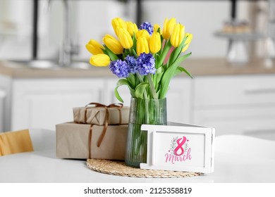 Greeting card with text 8 MARCH, flowers and gift boxes on dining table. International Women's Day celebration