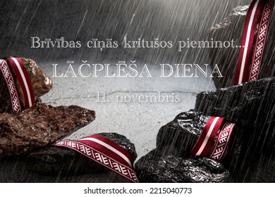 Greeting Card With Text In Latvian: In Memoriam Of Victims For Freedom Of Latvia. The Day Of National Hero Lacplesis.11 Of November.Lielvarde Belt And Flag Of Latvia Ribbon As Decoration On Wet Stones