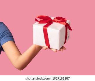 Greeting And Celebration Concept. Closeup of unrecognizable young woman holding and showing wrapped present box to camera, giving gift isolated over pastel pink studio background