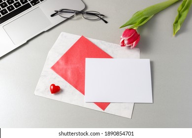 A Greeting Empty Card With An Envelope On A Grey Table With Red White Tulip Flower And A Laptop. At Home Or In The Office. Valentine Day Or Birthday Mockup Letter