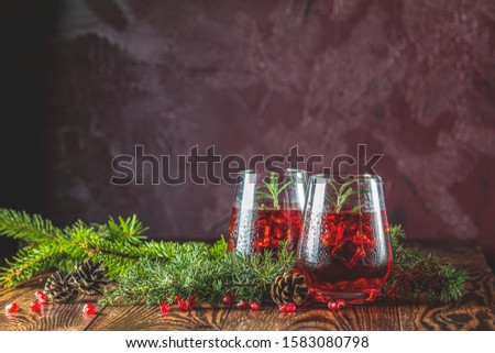 Greeting food Christmas and New Year composition. Two glasses of pomegranate drink surrounded  pine branches, claret bordeaux concrete background. Close up, shallow depth of the field.