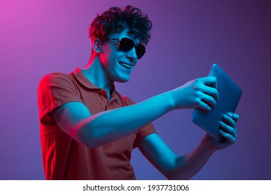Greeting friend online  Young man in sunglasses chating isolated multicolored background in neon light  Concept human emotions  facial expression  youth culture  digital life  Copy space for ad 