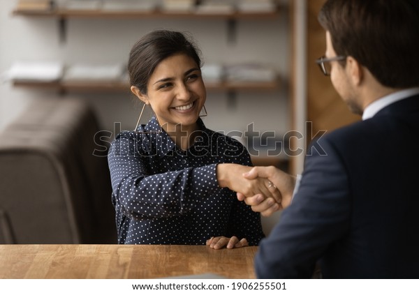 Greetings, you are hired. Happy young indian\
female successful job seeker shake hand of male hr manager being\
accepted on vacant place. Diverse business partners handshake close\
deal come to\
agreement