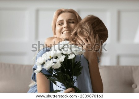 Greetings at your holiday, mommy. Excited happy young adult millennial mom straining little kid daughter to bosom receiving flowers and congratulations on Mothers Day or March 8 from beloved child