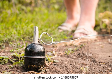 A grenade trap is on the ground. Improvised explosive device consists of a wire and a grenade tied to a ring. Female legs are in front of the mine. Selective focus