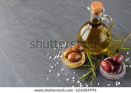 Grey abstract background with glass jar with olive oil and bowls with olives, sea salt and olive branch