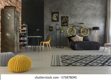 Grey apartment with bed, desk, chair, brick wall, yellow details