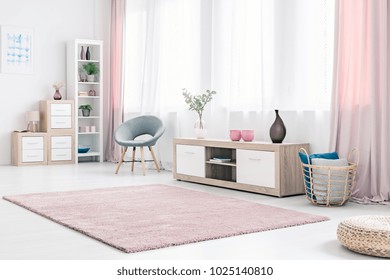 Grey Armchair Next To A Wooden Cupboard With Dark Vase In Spacious, Pink Living Room Interior