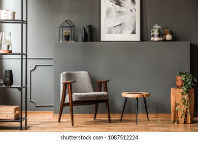 Grey armchair next to a wooden table in living room interior with plant and poster - Shutterstock ID 1087512224