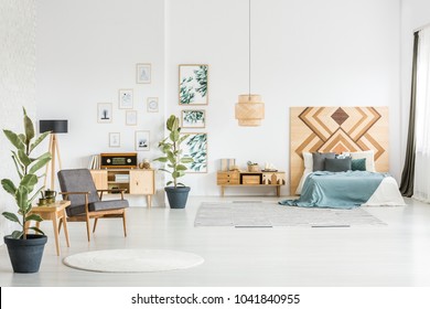 Grey Armchair In Spacious Vintage Bedroom Interior With Ficus And Green Bedding On Bed