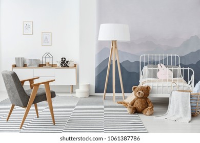 Grey armchair and wooden lamp on carpet in child's bedroom interior with plush toy and mountain wallpaper