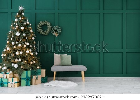 Grey bench and gift boxes under Christmas tree near green wall