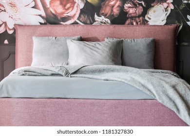 Grey Blanket And Cushions On Pink Bed In Feminine Bedroom Interior With Flowers Wallpaper. Real Photo