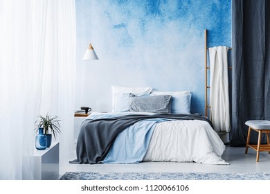 Grey And Blue Bedding On Bed In Spacious Bedroom Interior With Ladder And Plant