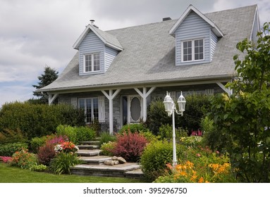 Grey brick with white trim cottage style Canadiana home facade with landscaped front yard in summer