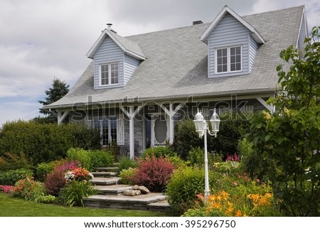 Grey brick with white trim cottage style Canadiana home facade with landscaped front yard in summer