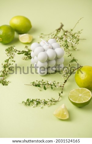 A grey bubble candle on a minty green background surrounded by limes and tree branches