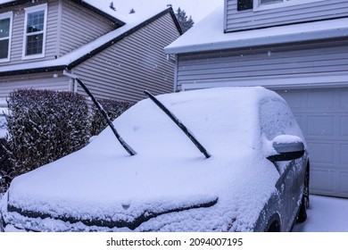 Grey Car Covered In Snow On A Driveway In Front Of The House With Front Wipers Lifted Up