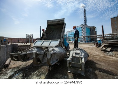 Grey Cement Dump Truck, Cement Bucket, Workers In Orange Hardhats. Smoke Chimney, Blue Industrial Building On Blue Sky. Developing Of Industrial Building.