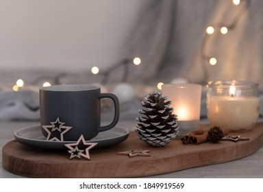 Grey coffee cup on a wooden board, cone, candles, cinnamon sticks, fairy lights and soft grey blanket together in a cozy autumn decoration with glitter wooden stars. Hygge concept. Soft focus bokeh.  - Powered by Shutterstock