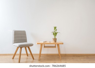 Grauer, bequemer Stuhl, der neben einem kleinen Tisch steht, mit einem Buch und einer Pflanze darauf in einem Tagungsraum