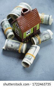 Grey Concrete Background With A Doll House And Rolls Of American Dollar Bills, Studio Shot, Elevated View