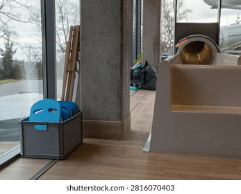 A grey crate holds blue floatation boards beside a large window in a contemporary water park facility, emphasizing clean organization for leisure activities and swimming pool equipment