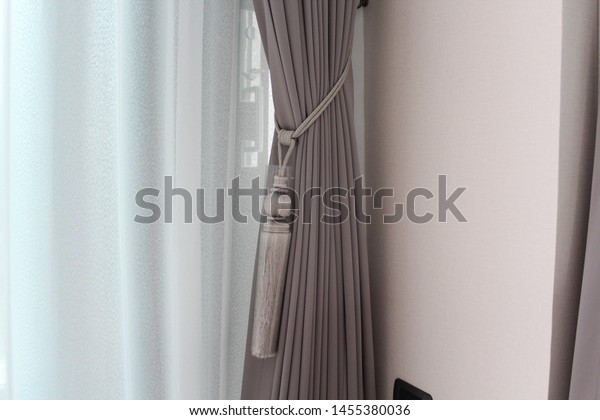 Grey\
curtains with white sheer curtains with luxury tie back in living\
room. Mood and tone are in grey and brown\
colour.