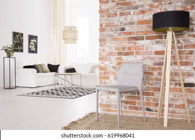 Grey designer chair and black lamp by the red brick wall