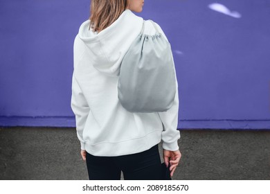 Grey Drawstring Pack Template, Mockup Of Bag For Sport Shoes On Woman's Shoulder Standing On A Violet Or Very Peri Background.