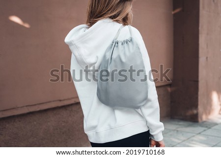 Grey drawstring pack template, mockup of bag for sport shoes on woman's shoulder. Back view, cropped.