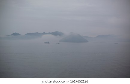 grey and foggy view of the bay near Hiroshima Japan, with low clouds, fishing boats,  and partially-occluded islands