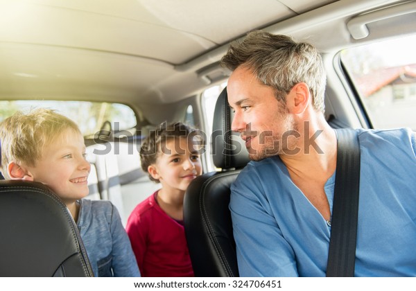 A grey hair father with beard is talking with his
two kids in the car. The ten years old brother and sister are
sitting in the back, they are wearing long sleeves shirts. The
father have his seat belt