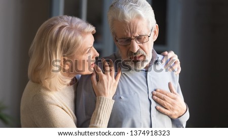 Grey haired man touching chest, having heart attack, feeling pain, suffering from heartache disease at home, mature woman supporting, embracing him, middle aged family, horizontal banner, close up