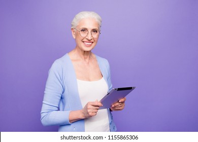 Grey Haired Old Smiling Business Woman Wearing Glasses, Reading Browsing Using Holding Tablet. Isolated Over Violet Purple Background