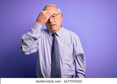 Grey haired senior business man wearing glasses standing over purple isolated background tired rubbing nose and eyes feeling fatigue and headache. Stress and frustration concept.
