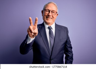 Grey haired senior business man wearing glasses and elegant suit and tie over purple background smiling looking to the camera showing fingers doing victory sign. Number two.