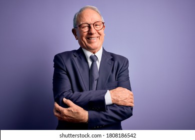 Grey Haired Senior Business Man Wearing Glasses And Elegant Suit And Tie Over Purple Background Happy Face Smiling With Crossed Arms Looking At The Camera. Positive Person.