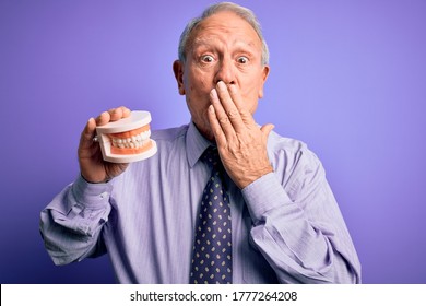 Grey Haired Senior Man Holding Orthodontic Prosthesis Denture Over Purple Background Cover Mouth With Hand Shocked With Shame For Mistake, Expression Of Fear, Scared In Silence, Secret Concept