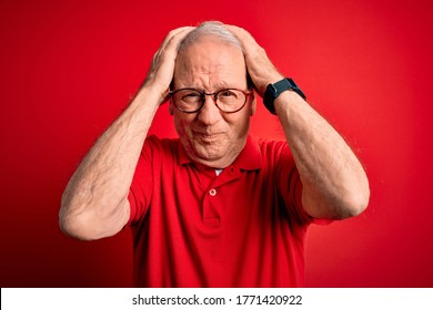 Grey haired senior man wearing glasses and casual t-shirt over red background suffering from headache desperate and stressed because pain and migraine. Hands on head.