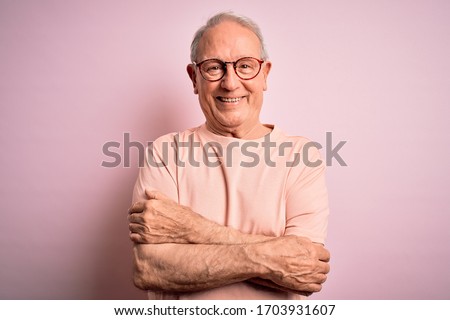 Grey haired senior man wearing glasses standing over pink isolated background happy face smiling with crossed arms looking at the camera. Positive person.