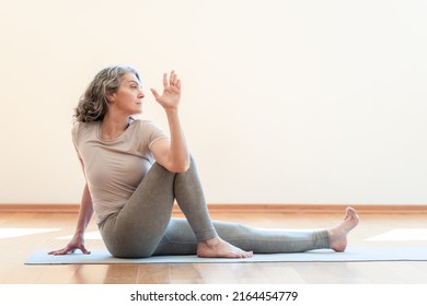 Grey haired woman doing seated twist exercises for health and a firmer body at home alone. Yoga and flexibility concept - Shutterstock ID 2164454779
