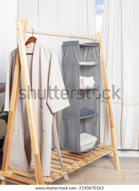 Grey hanging organizer for\
clothes and bathrobe on wooden floor hanger. Storage system for\
wardrobe