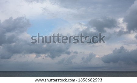 Grey high layered grey epic clouds on blue sky above thin sea water line. Heaven cloudscape air view