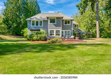 Grey house with long driveway lush green grass large yard and sunny woodendeck